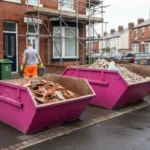Pink 6 yard and 8 yard builders skips with construction waste at a Manchester house renovation.